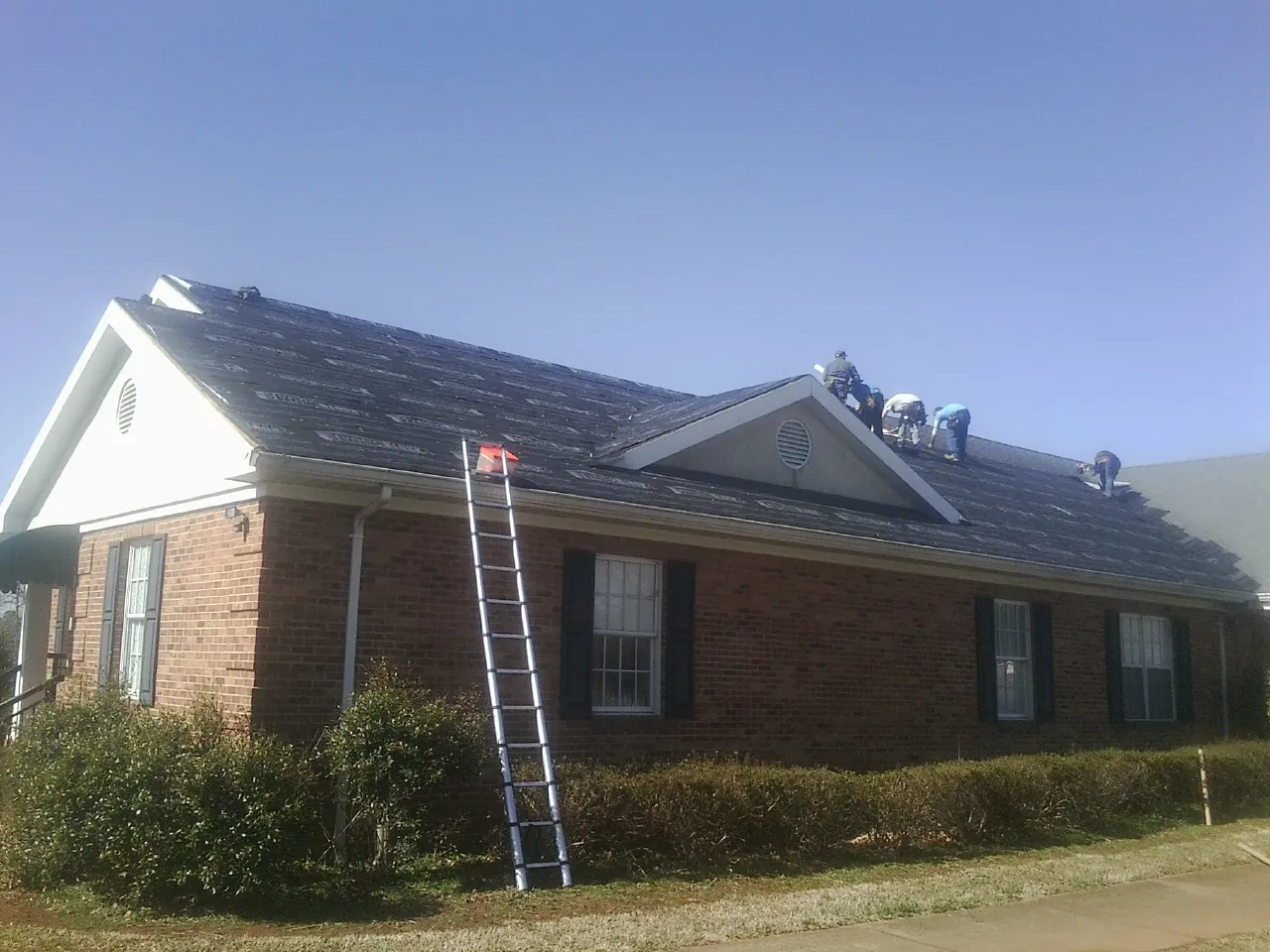 Crew tearing shingles off a brick ranch roof with a ladder set — Emergency Roof Repair work by our crew in South Glastonbury