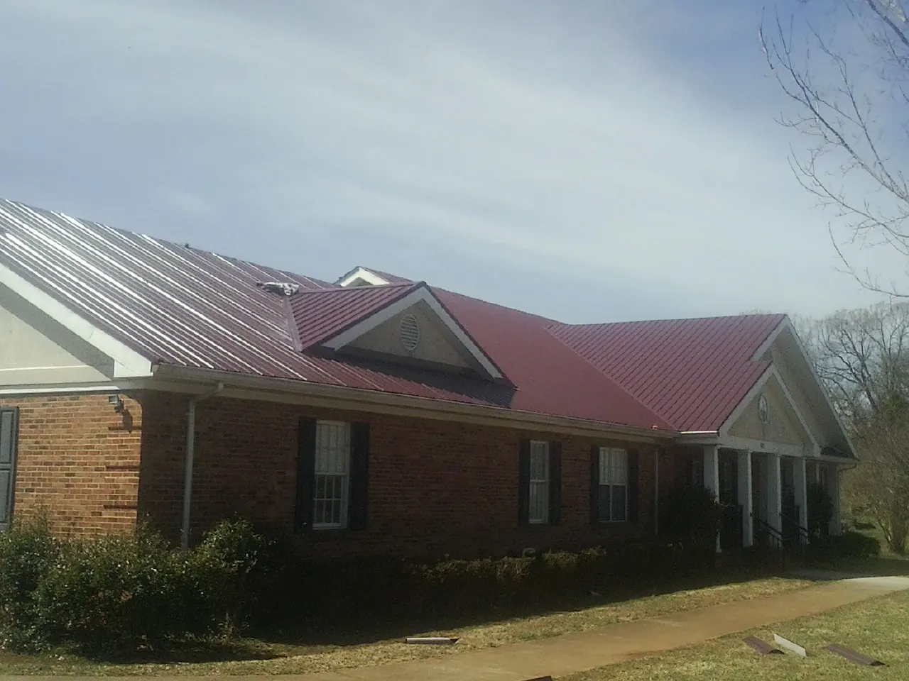 Red metal roof with gabled entries on a long brick building, from a Hail Damage Roof Repair job in South Glastonbury