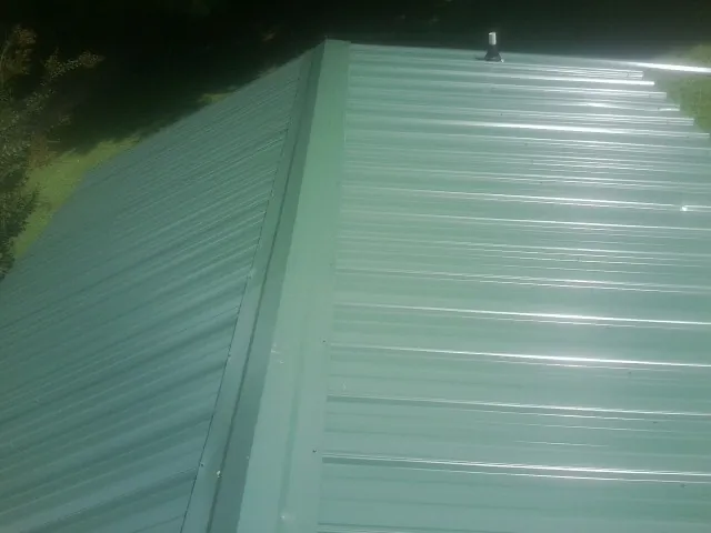 New green metal panels meeting at the ridge of a roof — Flat Roof Repair work by our crew in South Glastonbury