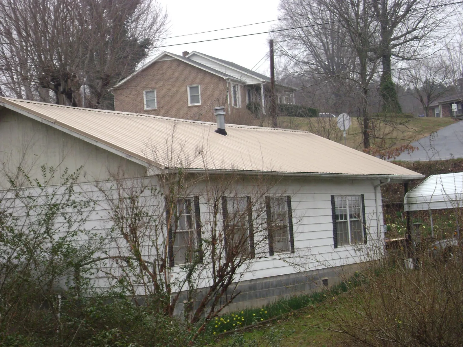 Tan metal roof on a white sided house set into a hillside — Commercial Roofing by Roofing Brothers in South Glastonbury